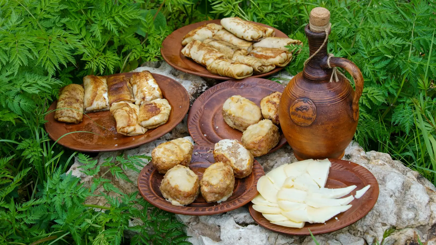 Plăcinte și brânză pe farfurii de lut, cu o carafă de ceramică, pe iarbă