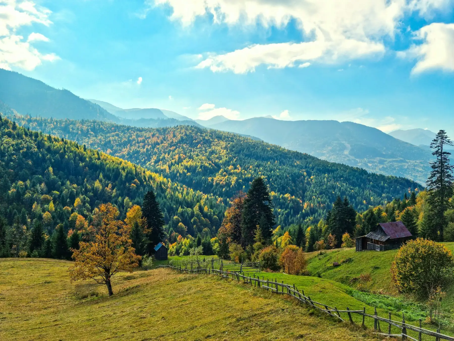 Vale cu păduri de toamnă, o casă din lemn și munți în depărtare